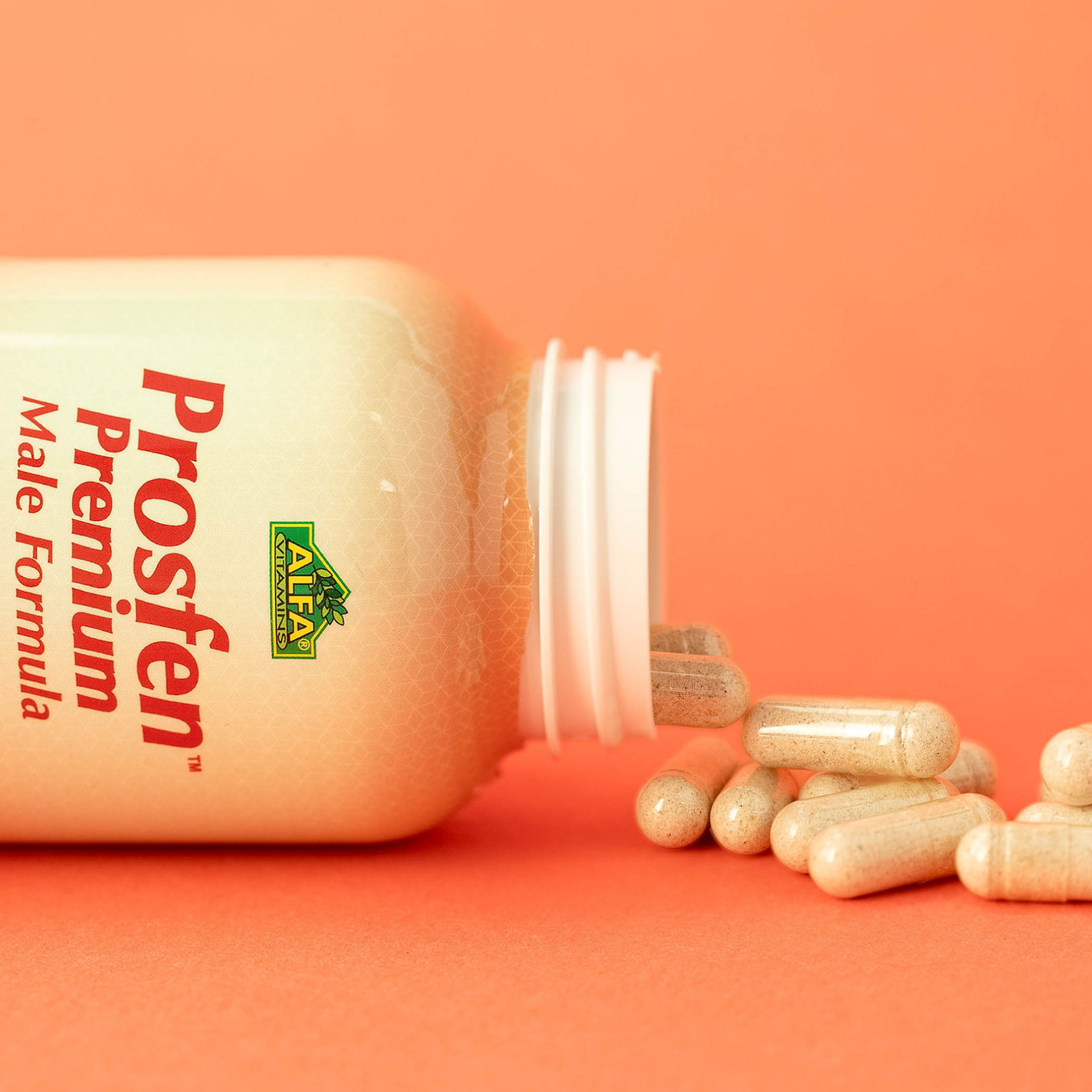 A bottle of Prosfen Premium Male Formula - 120 capsules, by Alfa Vitamins, lies on its side with capsules spilling onto an orange surface. The label showcases Saw Palmetto for prostate support among its potent herbal extracts.