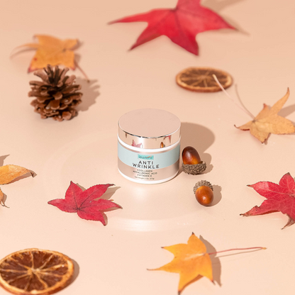 A 2 oz jar of Anti Wrinkle Cream by Lawrens Cosmetics from Alfa Vitamins Store sits at the center, encircled by autumn leaves, acorns, dried orange slices, and a pinecone on a light background for a fall-themed display.