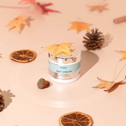 A 4oz jar of Alfa Vitamins Store Day Cream with Caviar Extract is surrounded by autumn leaves, pine cones, dried citrus slices, and an acorn, creating a fall-themed arrangement on a light surface.