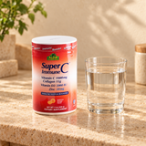 Closed Alfa SuperC Immune orange flavor 11 oz canister on a warm stone counter beside a plain water glass.