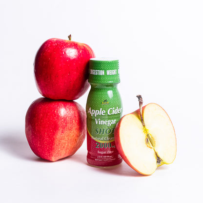 A compact green bottle labeled Apple Cider Vinegar Shot 2000 MG - 20 Pack from Alfa Vitamins Store sits beside two whole red apples and a sliced half, displaying its core. Ideal for health enthusiasts or supplement seekers, this scene is set against a plain white backdrop.