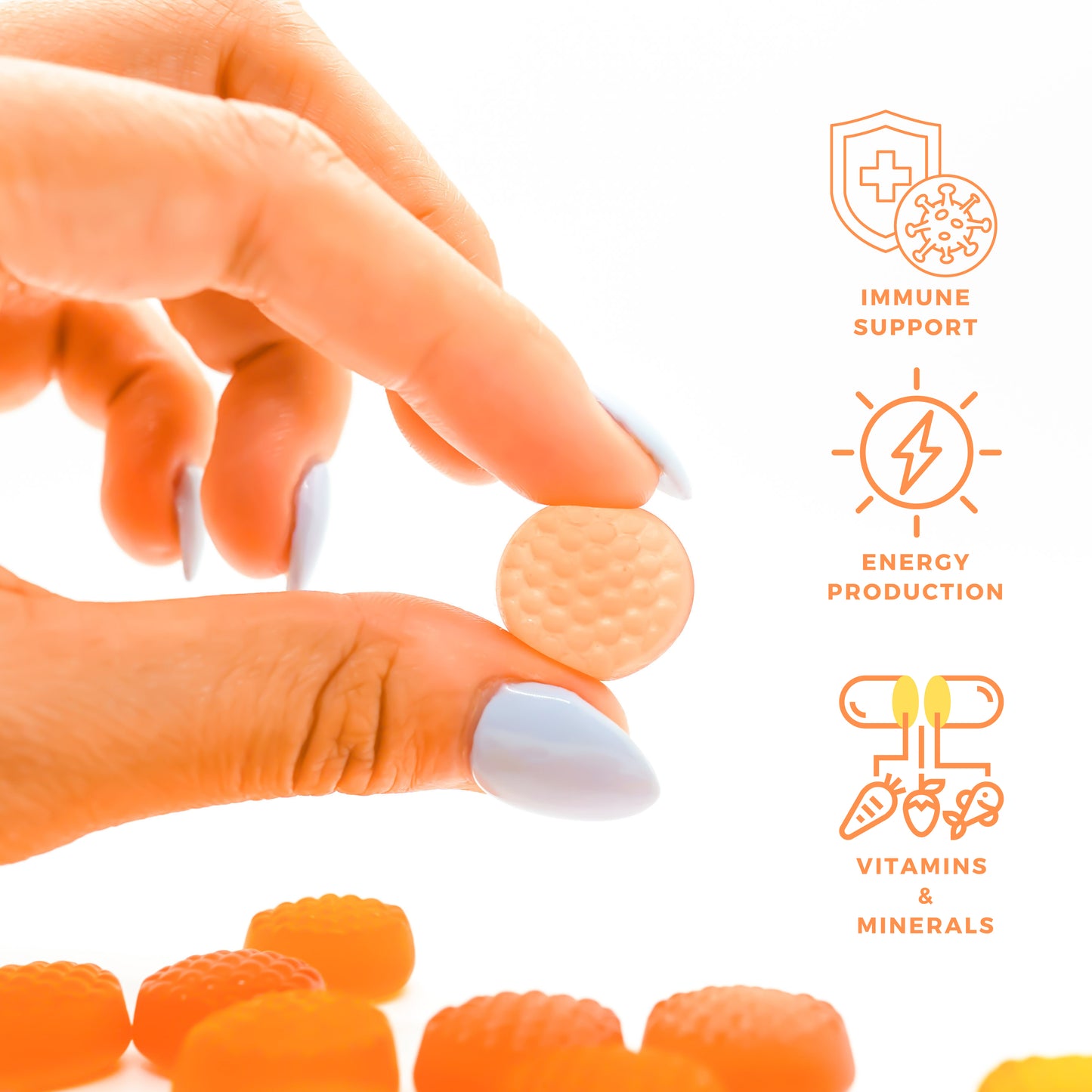 A hand with blue nails holds an orange gummy from Alfa Vitamins Stores MultiVitamins for Adults - Orange Flavor. Benefits like immune support and energy production surround it, while more gummies, packed with essential vitamins and minerals, are scattered below, showcasing their nutritious charm.