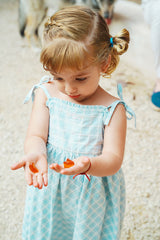 Young child in a blue checkered dress looking at orange gummies held in both hands.
