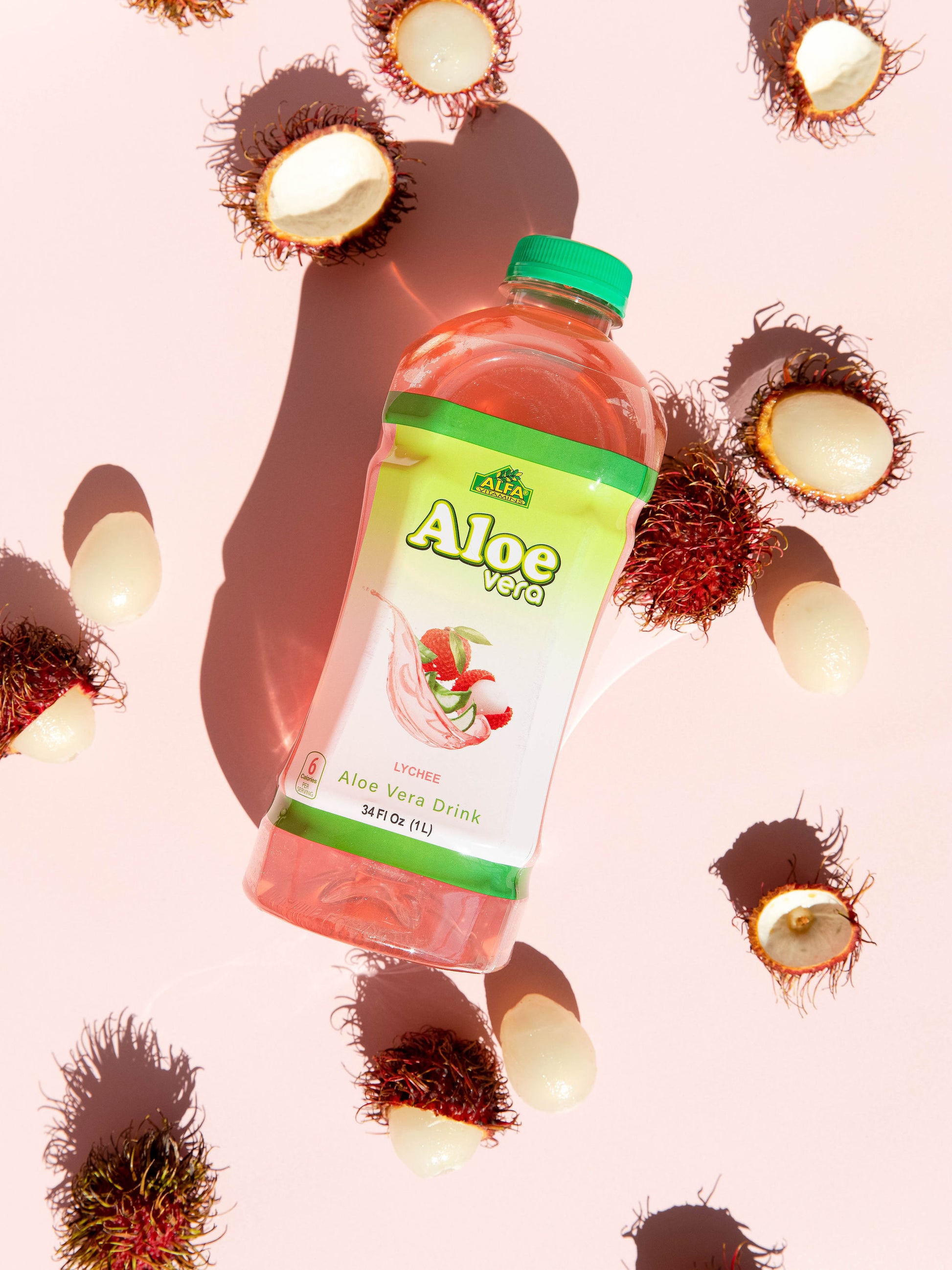 An Alfa Vitamins Aloe Vera Drink-Lychee bottle with a green cap sits among whole and halved rambutans on a light pink surface, casting a shadow. The rambutans spiky exteriors and white flesh highlight Aloe Veras digestive benefits.