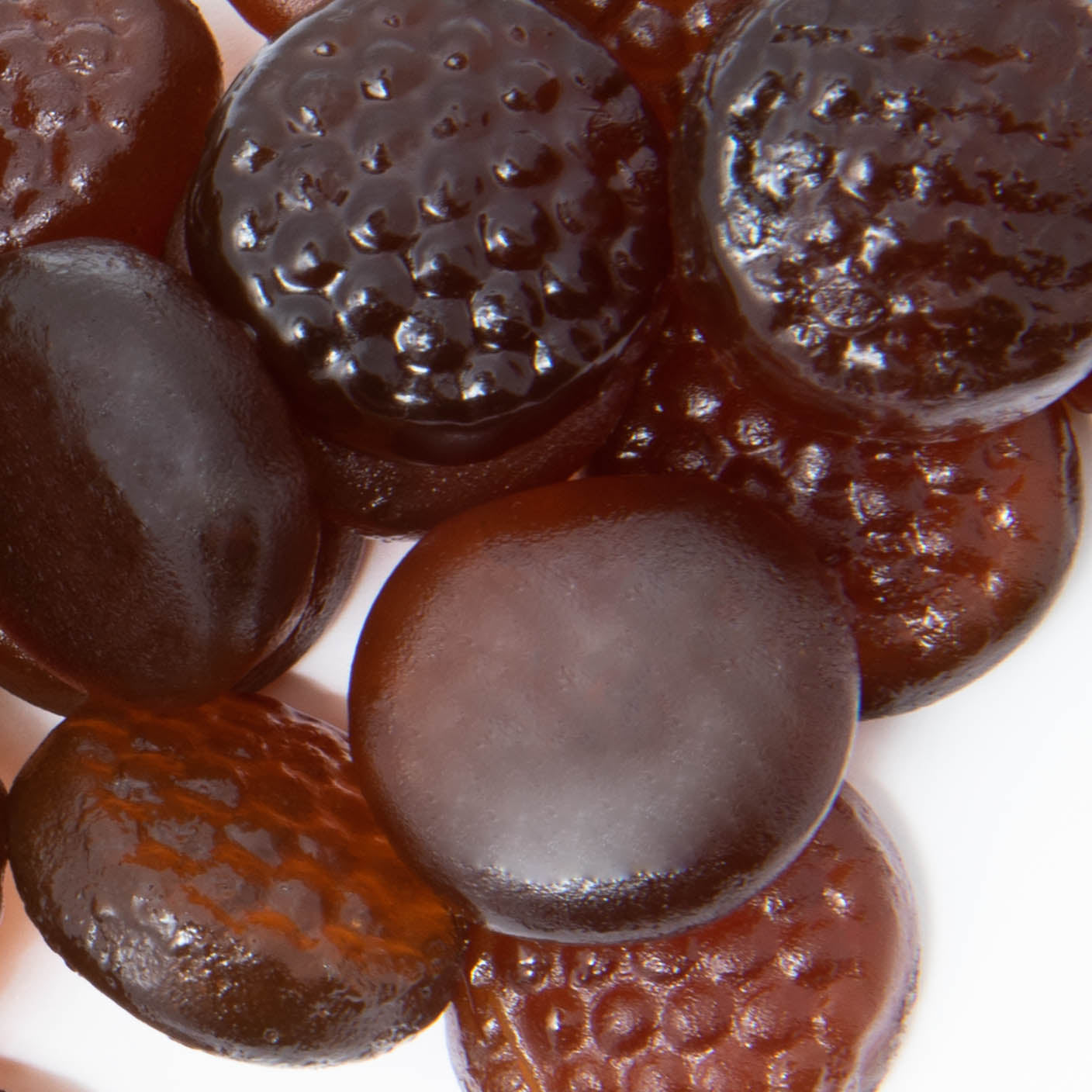 Close-up of assorted dark brown B Complex Gummies from Alfa Vitamins Store, showing smooth and dimpled textures. These 60 gummies, designed to support the immune system, are displayed on a white surface.