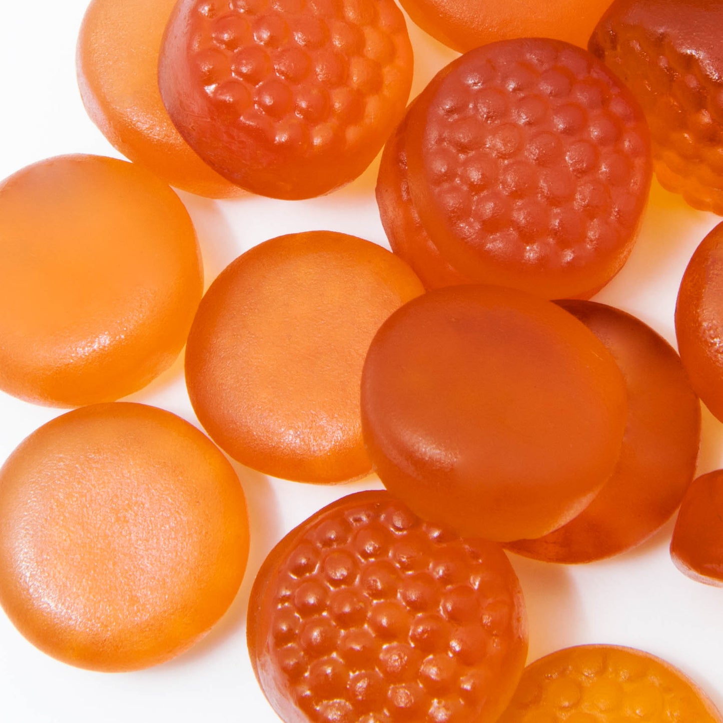 A close-up of Alfa Vitamins Stores vibrant orange MultiVitamins for Adults - Orange Flavor 60 Gummies on a white surface. These adult multivitamins, rich in essential nutrients, range from light to dark orange with smooth and textured finishes, making them an appealing choice.