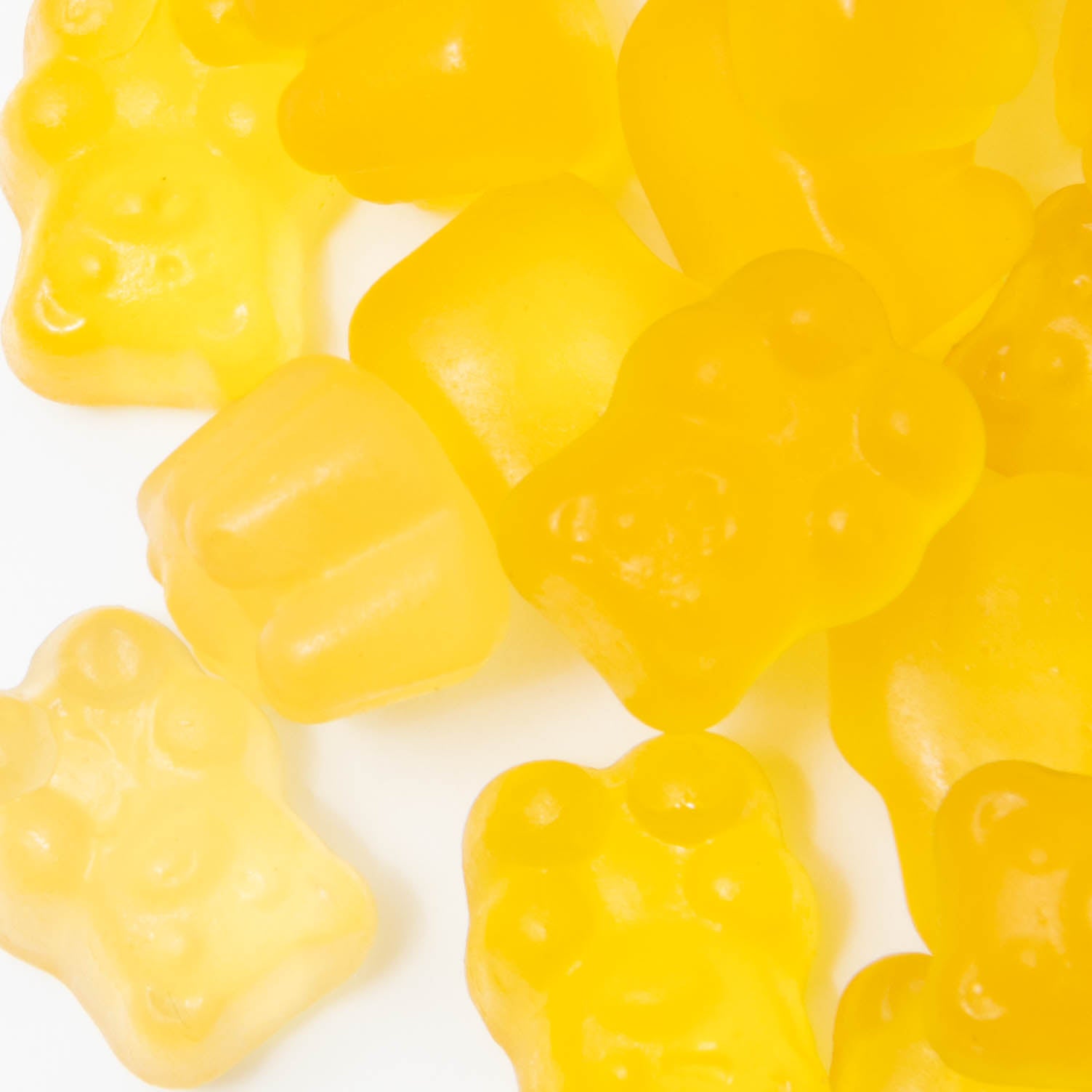 Close-up of scattered yellow Omega 3 Adult Gummies by Alfa Vitamins Store, shaped like bears and fruit, on a white surface.