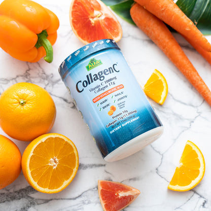 A container of Alfa Vitamins CollagenC Peptides Hydrolysate Powder (11 oz) sits on a marble surface, surrounded by fresh orange slices, an orange bell pepper, whole oranges, and carrots. The packaging highlights benefits for hair, nails, skin rejuvenation, and joint mobility.